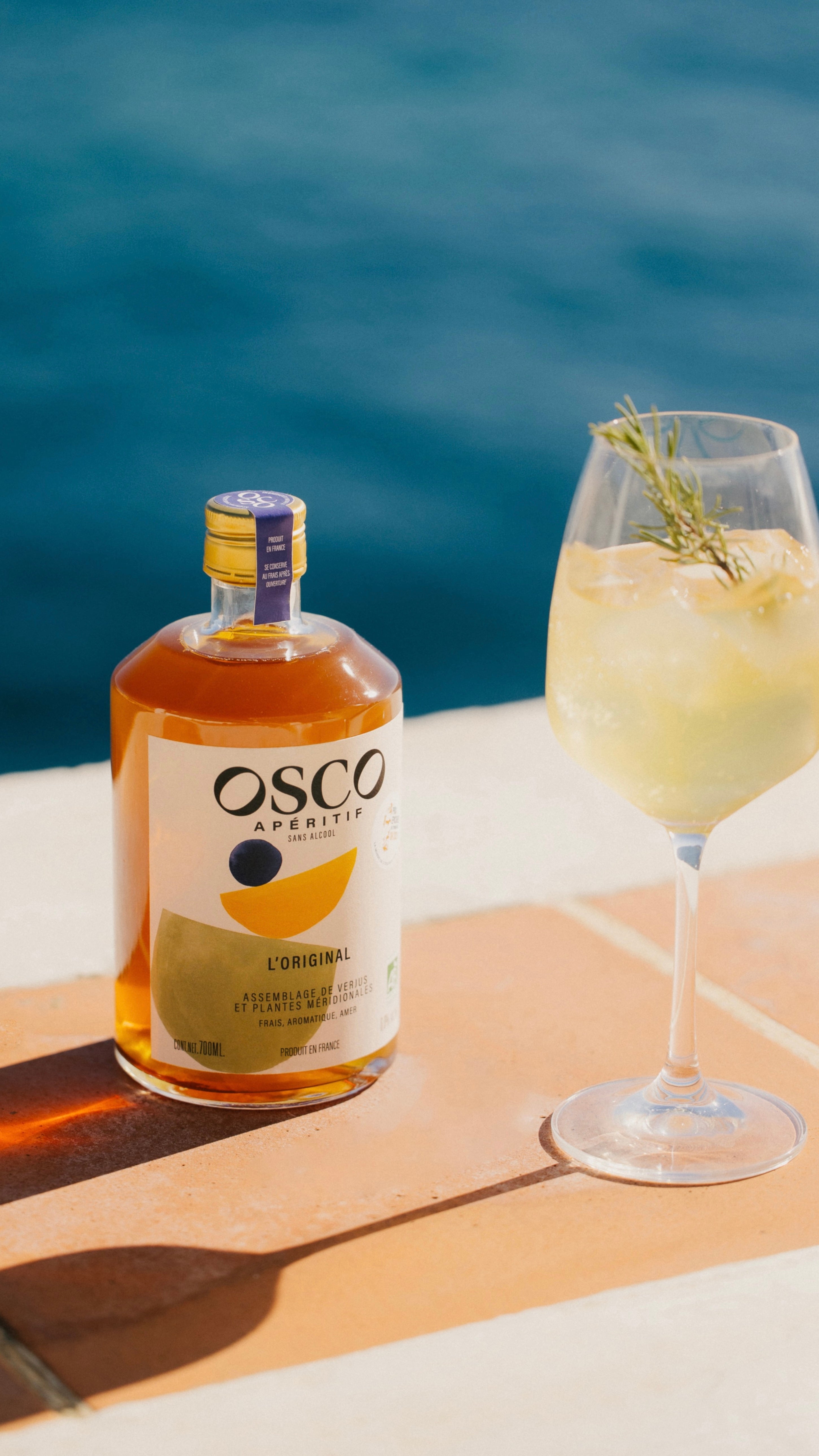 Bouteille d’OSCO L’Original , apéritif sans alcool botanique aux notes d’agrumes et d’amertume, présentée en extérieur lumineux pour un apéritif élégant et moderne.